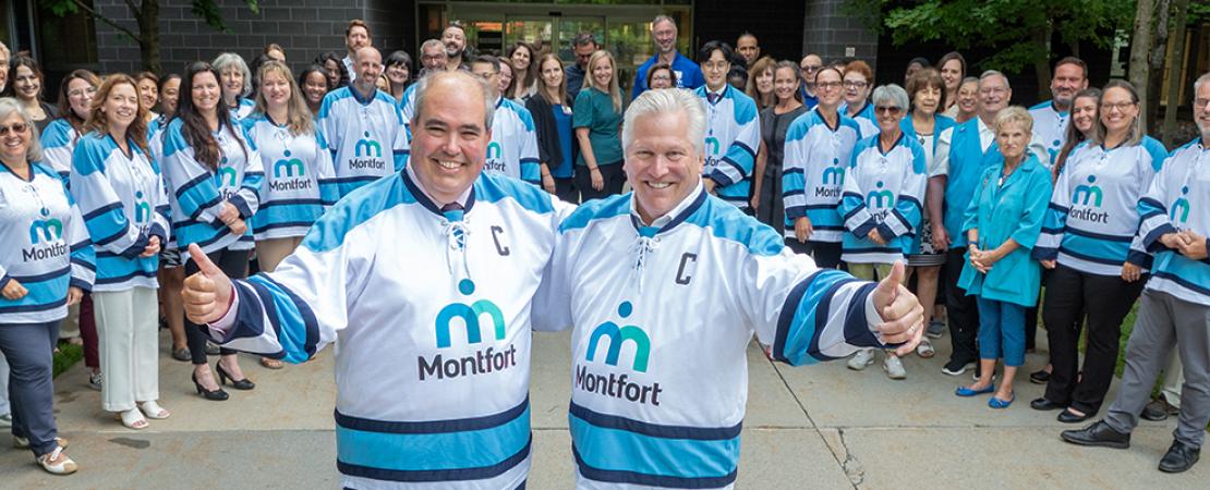 Dominic Giroux et Dr B. Leduc arborant un chandail à l'effigie de Montfort devant un groupe d'employés